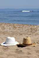 Zwei Strohhüte liegen am Strand