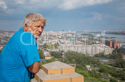 the elderly man looks at a city and the river