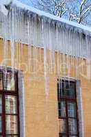 snow-covered roof with big icicles in winter day