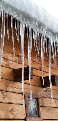 wooden house with big icicles on snow-covered roof