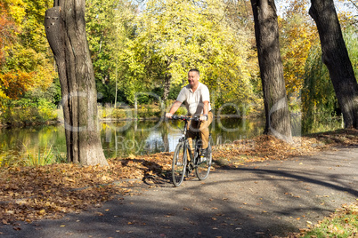 man rides his bike through the park in autumn