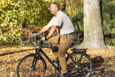 man rides his bike through the park in autumn