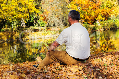 man sitting in autumn leaves by the lake