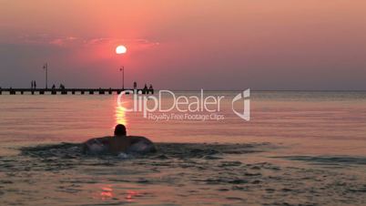 man swimming in the sea at sunset