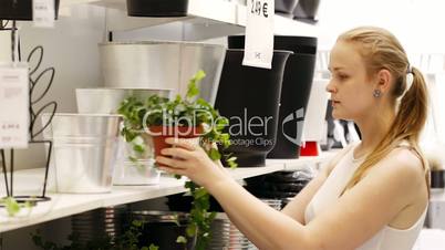 Young blond woman looking at vases with plants in a shop