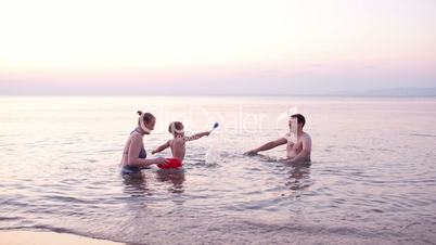 Young family playing red toy boat at sunset