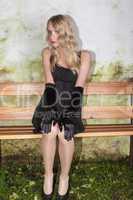 junge frau mit langen blonden haaren und eleganten minikleid sitzt auf einer bank