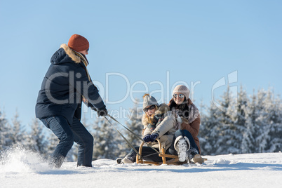 young man pulling girls on winter sledge