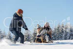 young man pulling girls on winter sledge