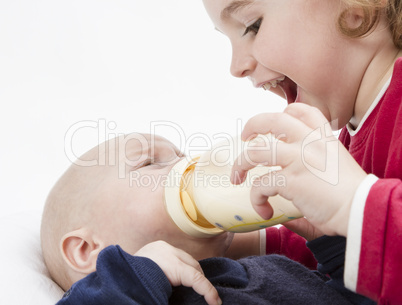 young child feeding toddler with milk bottle