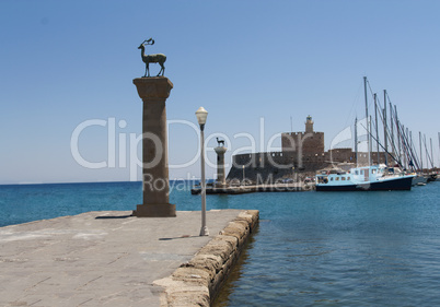 rhodes mandraki harbor with castle and symbolic deer statues, greece