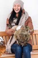 young woman stroking cat sitting winter bench