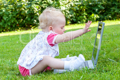 baby sitting with laptop in a meadow