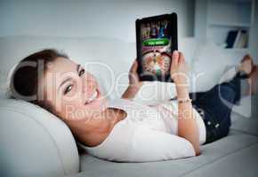 Happy woman lying on couch and gambling on tablet