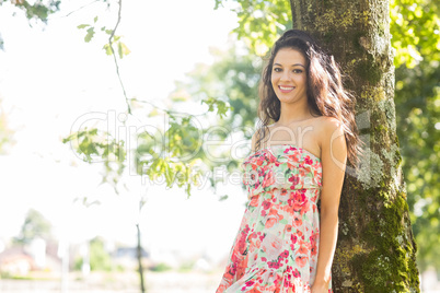 Stylish smiling brunette leaning against tree