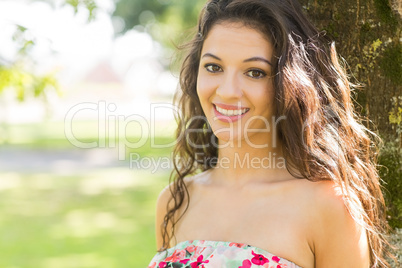 Stylish cheerful brunette leaning against tree