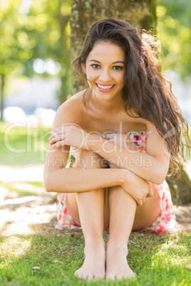 Stylish smiling brunette sitting under a tree