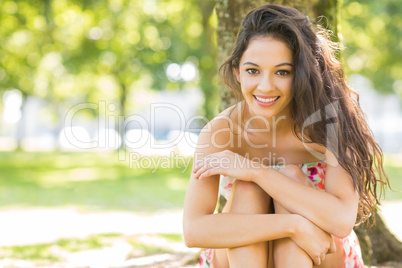 Stylish cheerful brunette sitting under a tree