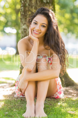 Stylish happy brunette sitting under a tree