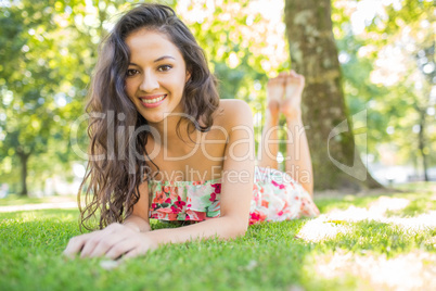 Stylish smiling brunette lying on a lawn looking at camera