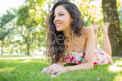 Stylish cheerful brunette lying on a lawn looking away