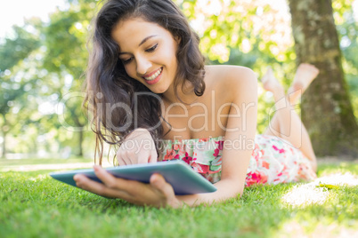 Stylish cheerful brunette lying on a lawn using tablet