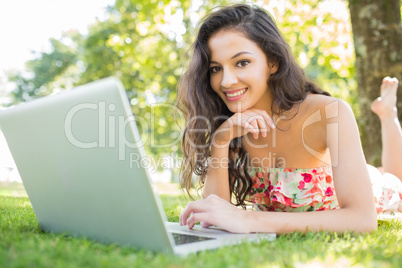Stylish cheerful brunette lying on a lawn using laptop
