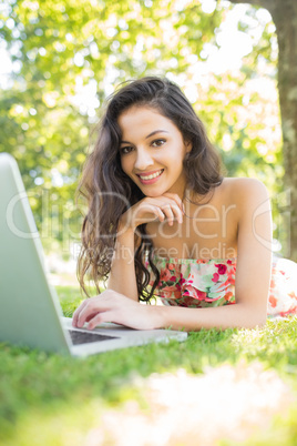 Stylish smiling brunette lying on a lawn using laptop