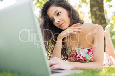 Stylish thoughtful brunette lying on a lawn using laptop