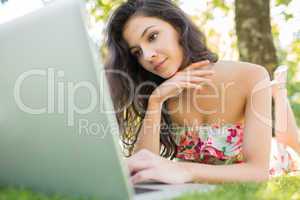 Stylish thoughtful brunette lying on a lawn using laptop