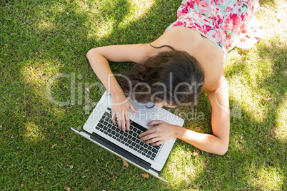 Stylish brunette lying on the grass typing at her laptop