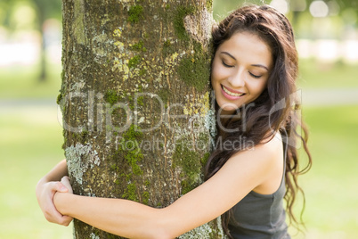 Casual cheerful brunette embracing a tree with closed eyes