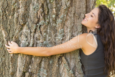 Casual content brunette embracing a tree with closed eyes