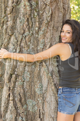 Casual attractive brunette embracing a tree looking at camera