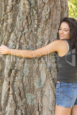 Casual beautiful brunette embracing a tree with closed eyes