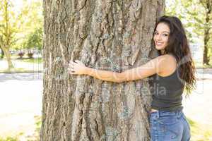 Casual gorgeous brunette embracing a tree looking at camera