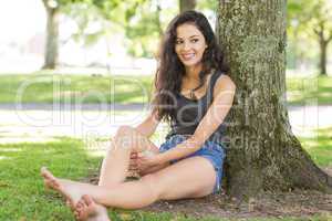 Casual happy brunette sitting leaning against tree
