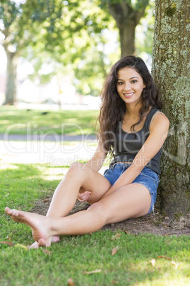 Casual smiling brunette sitting leaning against tree