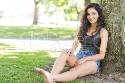 Casual attractive brunette sitting leaning against tree