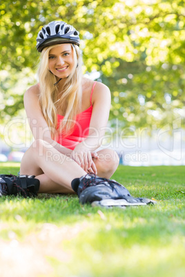 Casual cheerful blonde wearing inline skates and helmet sitting