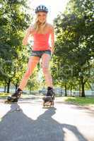 Casual smiling blonde inline skating on pathway