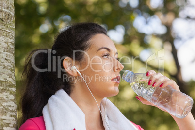 Ponytailed brunette woman drinking and leaning against a tree