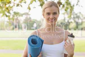 Cheerful blonde woman posing holding an exercise mat