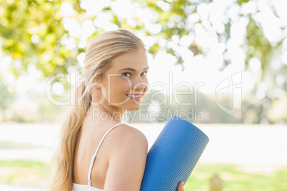 Beautiful sporty woman posing holding an exercise mat