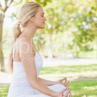 Side view of ponytailed calm woman meditating sitting in a park