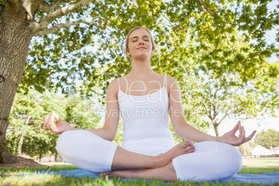 Front view of beautiful young woman sitting in a park meditating