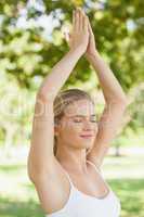 Fit woman doing yoga with hands raised in prayer in a park