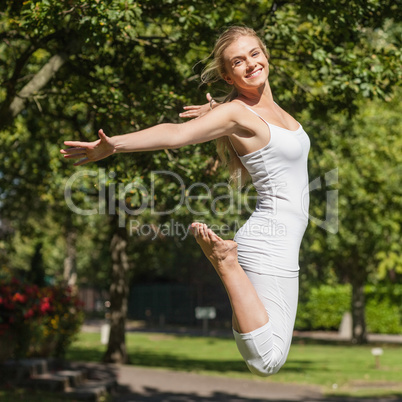 Side view of young fit woman jumping spreading her arms