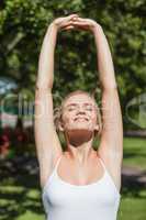 Young fit woman stretching her arms standing in a park