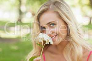 Beautiful blonde woman smelling a flower sitting in a park